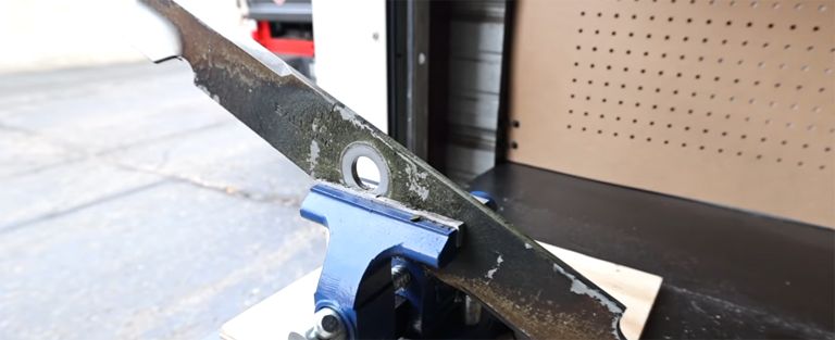 A lawn mower blade held in a vice ready to be sharpened